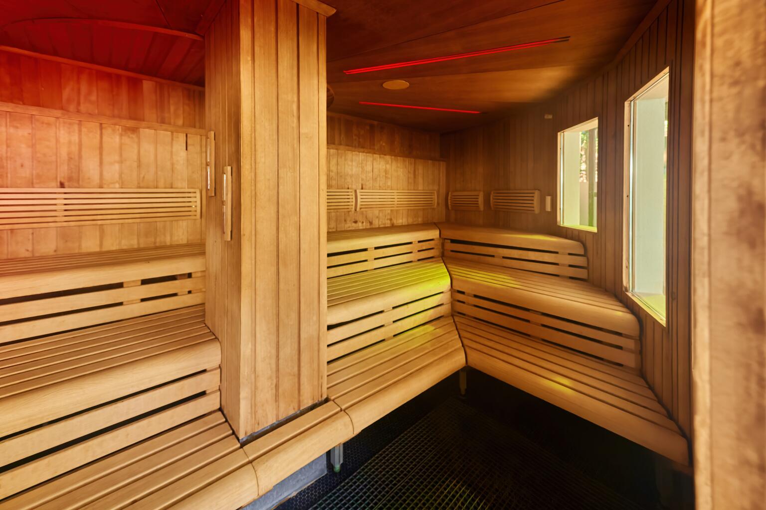 Innenansicht einer modernen Holzsauna mit mehreren Sitzbänken auf zwei Ebenen, warm beleuchtet mit roten Lichtakzenten an der Decke.