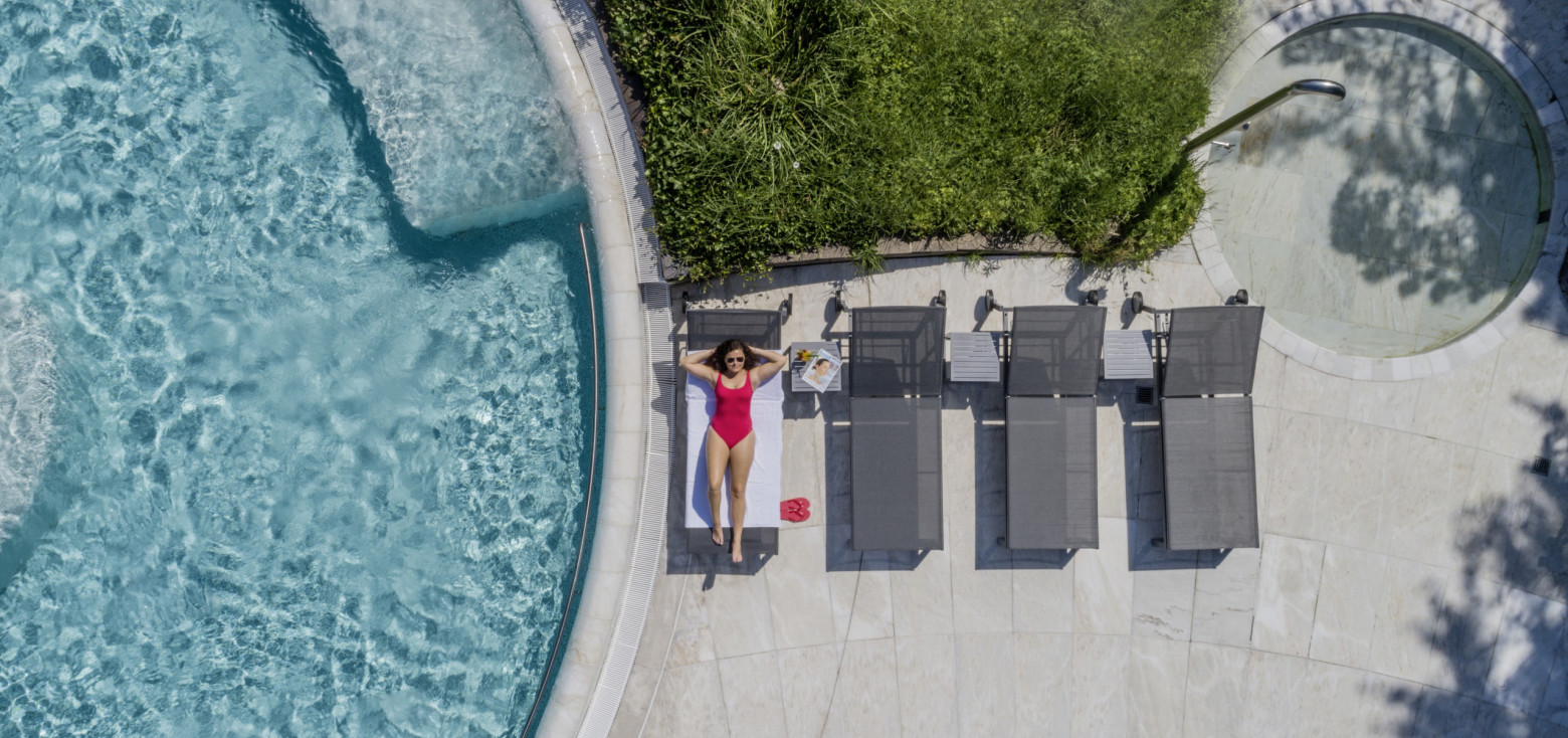 Frau in pinkem Badeanzug entspannt auf grauer Sonnenliege am Beckenrand der Caracalla Therme Baden-Baden, Sommeraufnahme.